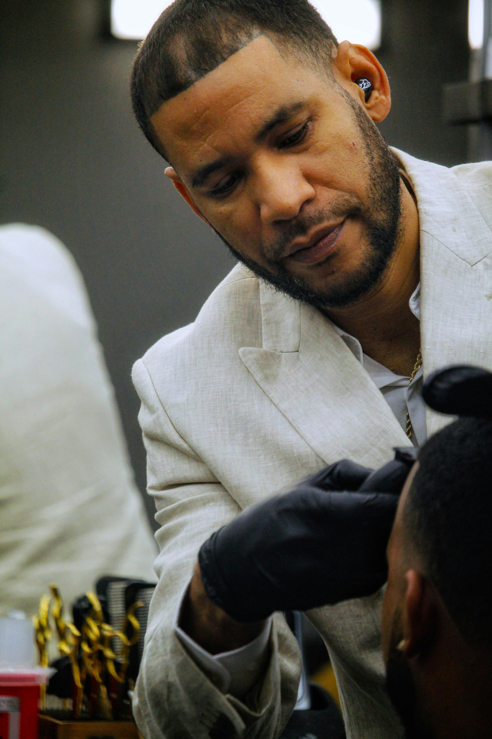 A skilled barber in a white suit precisely trims a client's hair in a modern barbershop.