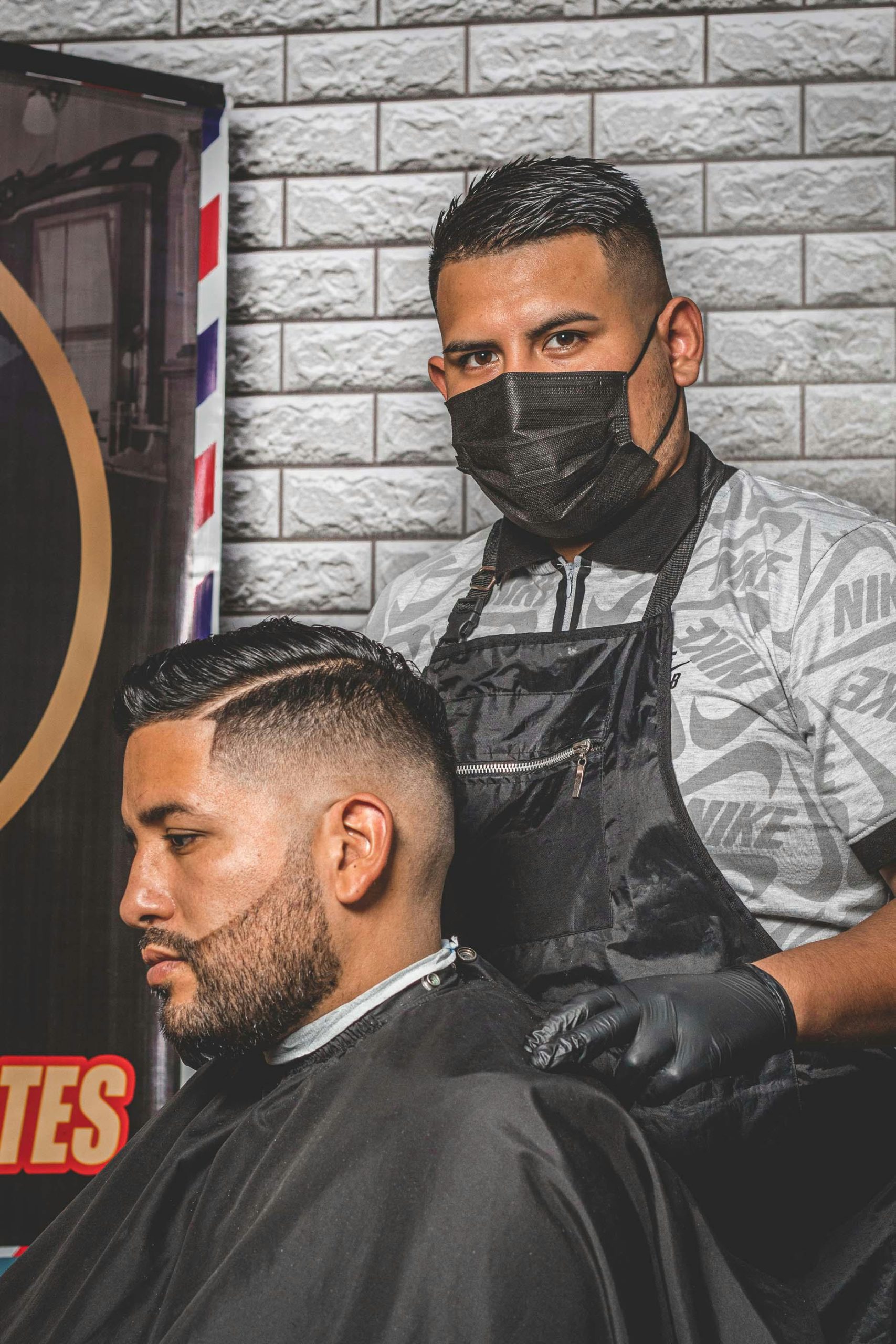 Barber in black apron and gloves expertly cutting a man's hair in a modern salon setting.